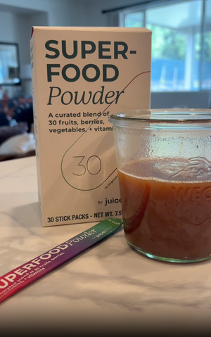 Superfood powder packaging with a glass of red liquid on a table.